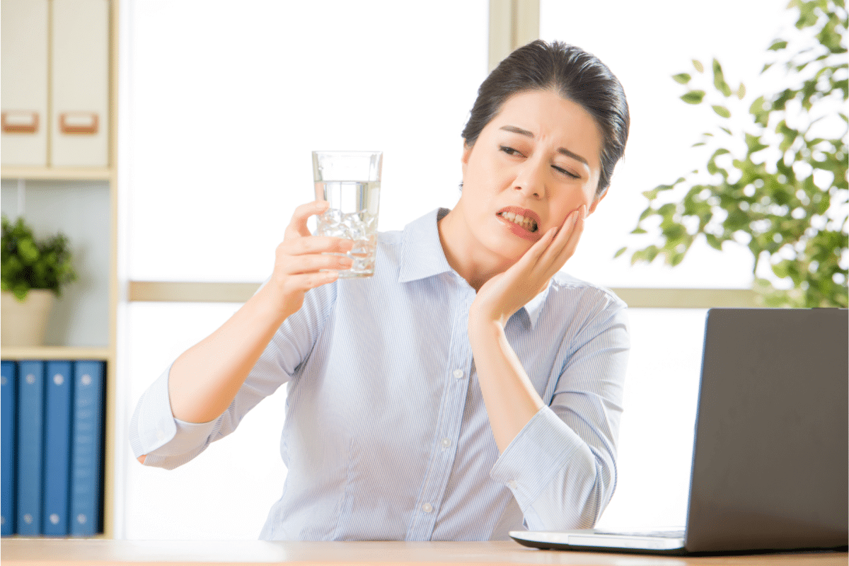 Asian woman with tooth sensitivity looking at cold water