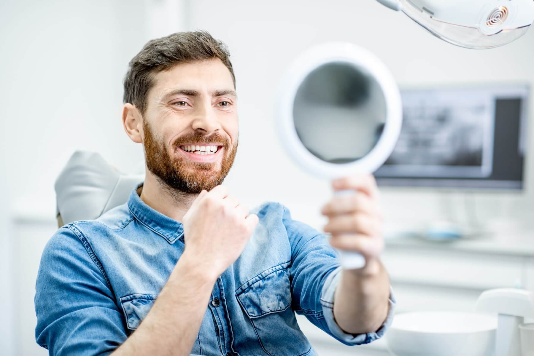 man smilling and looking at mirror in dentist chair